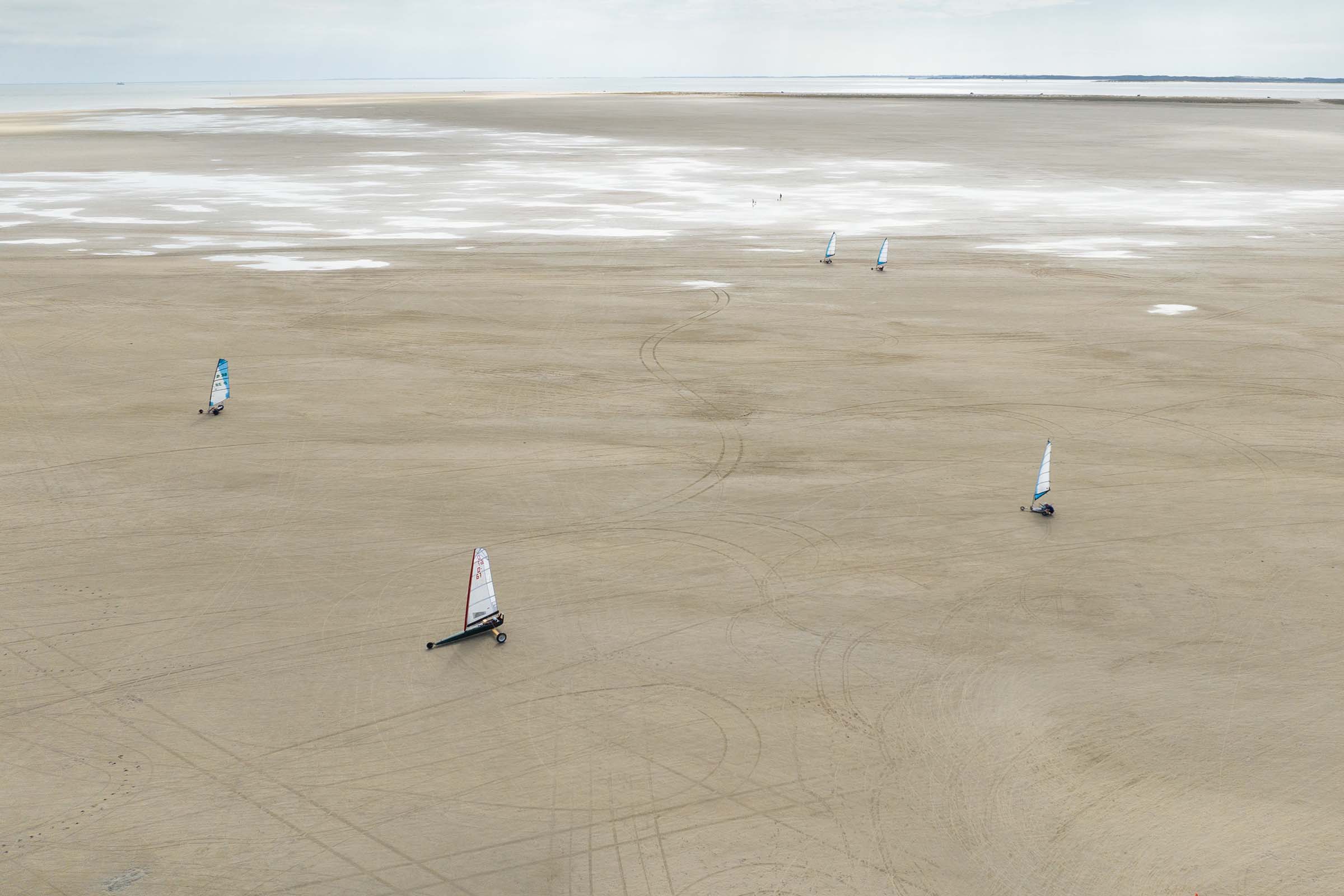 Case Stedet Tæller X, dronefoto, vind i sejlet, biler på strand.