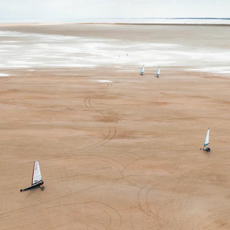 Dronebillede af en vindsejlende bil der kører på sandet i Jylland.
